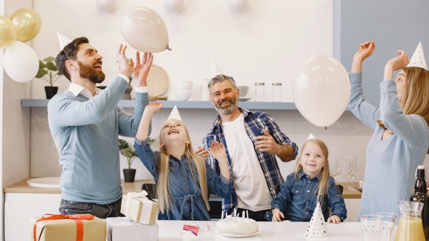 A happy family celebrating together indoors with balloons, cake, and gifts.